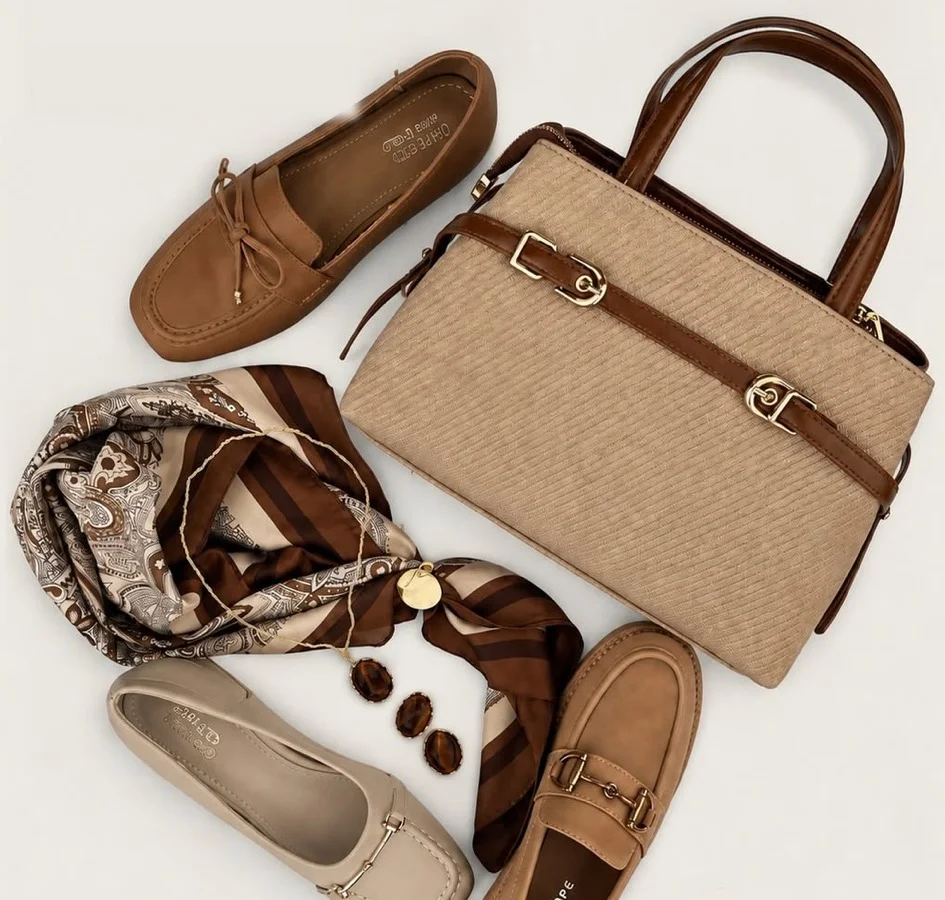 A straw-effect tote, loafers, a silk scarf and jewellery laid out on cream
